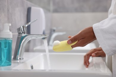 Photo of Young man cleaning face sponge above sink in bathroom, closeup