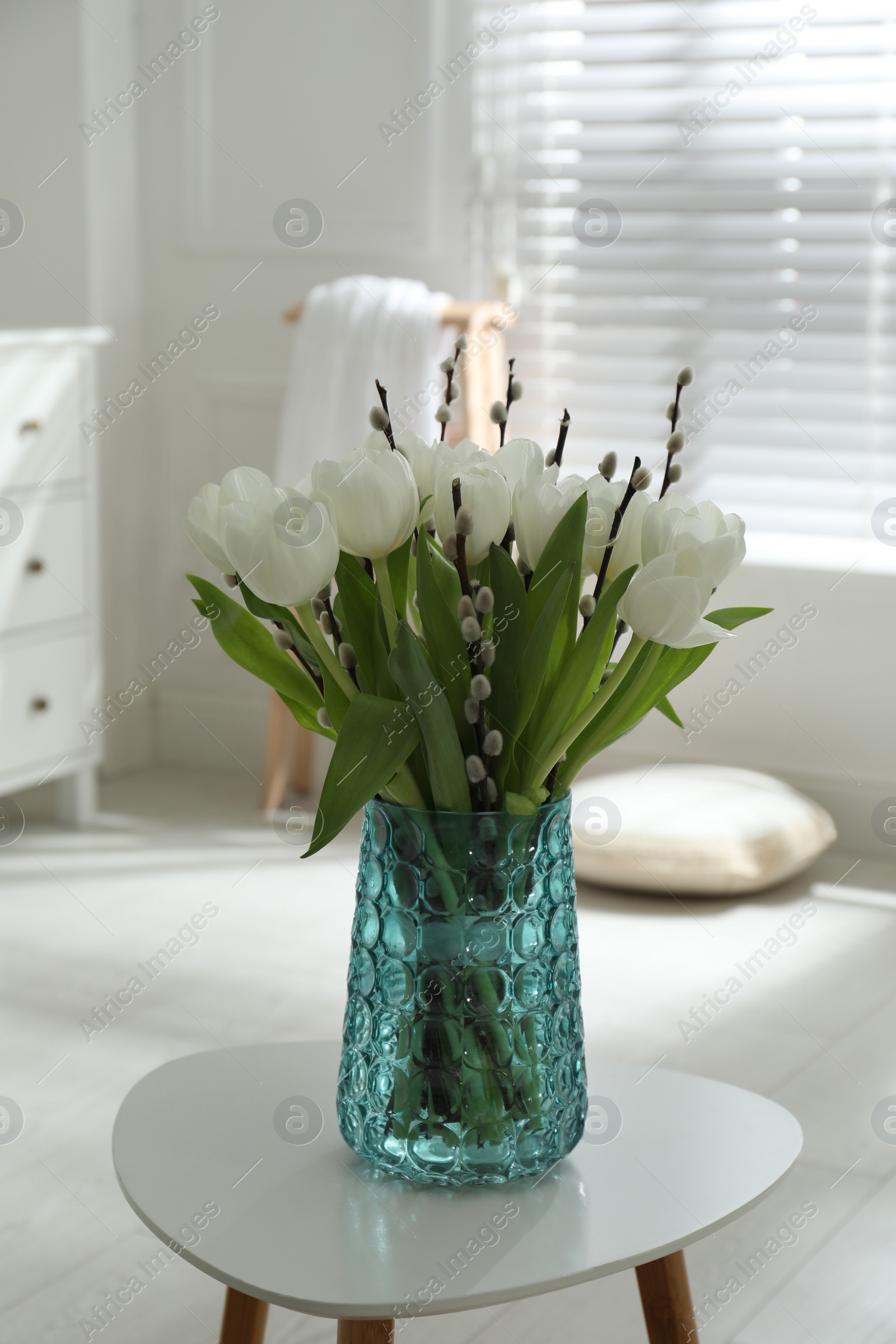 Photo of Beautiful bouquet of willow branches and tulips in vase on table indoors