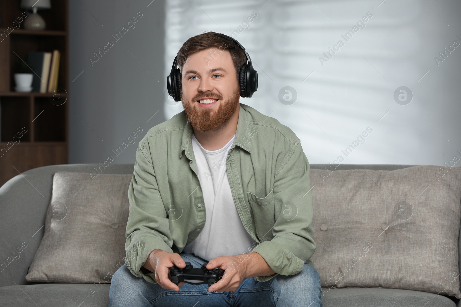 Photo of Happy man in headphones playing video game with controller at home