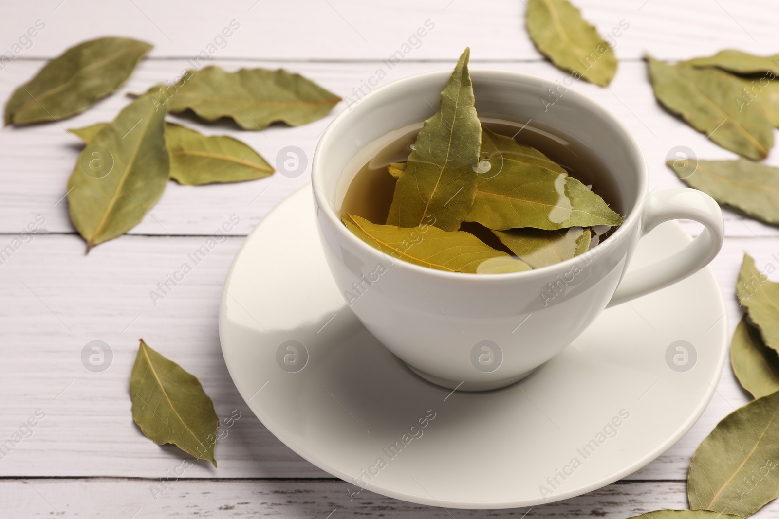 Photo of Cup of freshly brewed tea with bay leaves on white wooden table, closeup