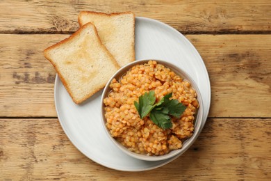 Photo of Delicious red lentils with parsley in bowl served on wooden table, top view