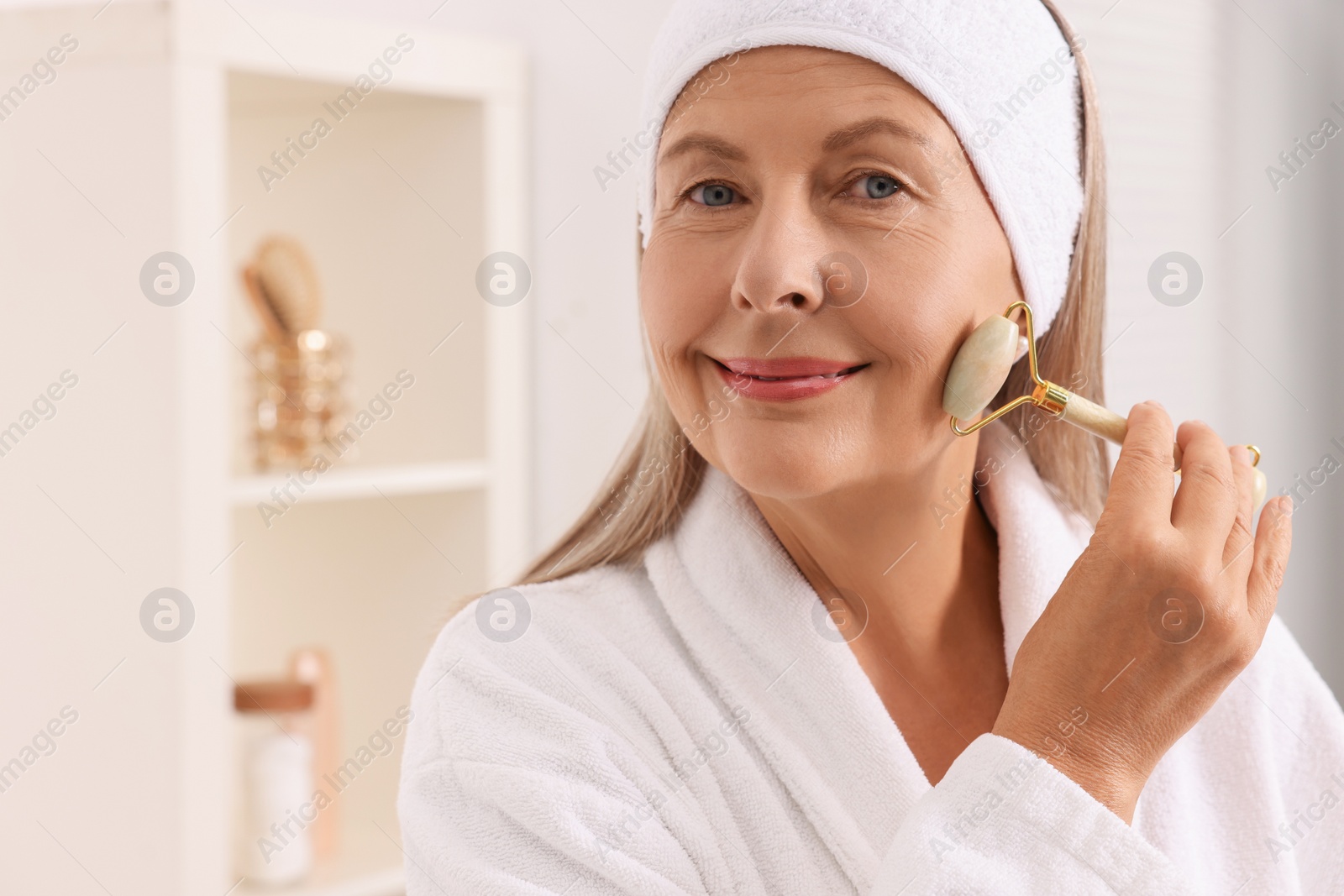 Photo of Woman massaging her face with jade roller in bathroom. Space for text