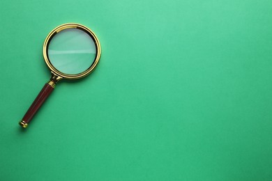 Photo of Magnifying glass on green background, top view. Space for text