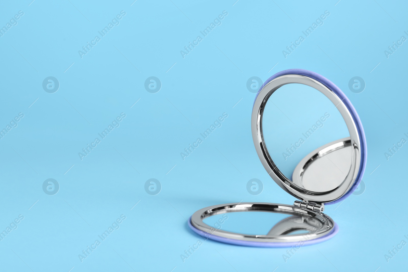 Photo of Stylish cosmetic pocket mirror on light blue background. Space for text