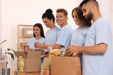 Photo of Group of volunteers packing food products at table in warehouse