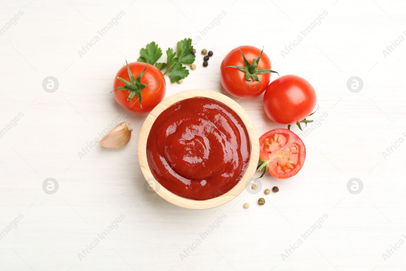 Photo of Delicious ketchup in bowl, peppercorns and tomatoes on white wooden table, flat lay