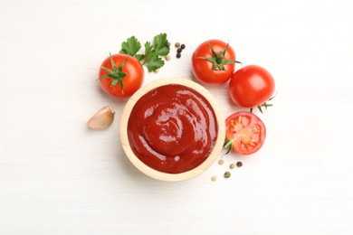 Photo of Delicious ketchup in bowl, peppercorns and tomatoes on white wooden table, flat lay