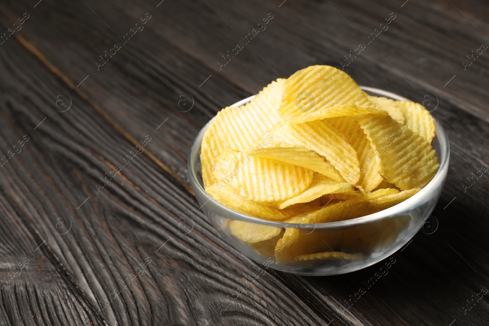 Photo of Bowl of potato chips on wooden table. Space for text