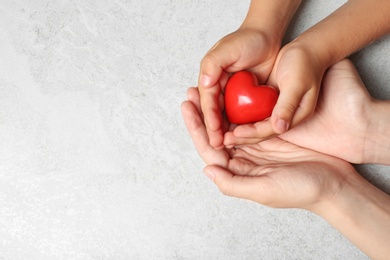 Photo of Woman and child holding heart on grey stone background, top view with space for text. Donation concept