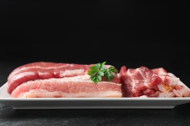 Photo of Pieces of raw pork belly and parsley on black textured table, closeup. Space for text