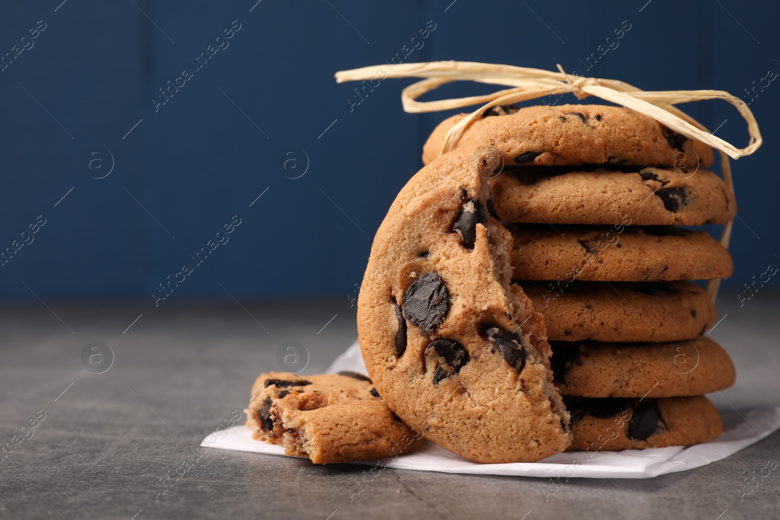 Photo of Stack of delicious chocolate chip cookies on grey table, closeup. Space for text