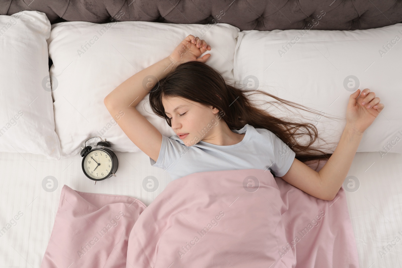 Photo of Beautiful little girl with alarm clock sleeping in bed, top view