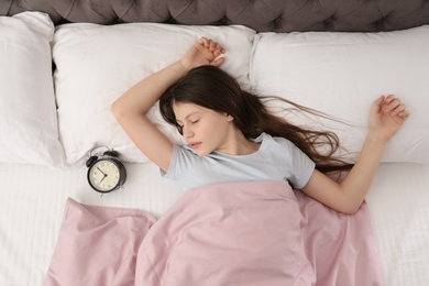 Beautiful little girl with alarm clock sleeping in bed, top view