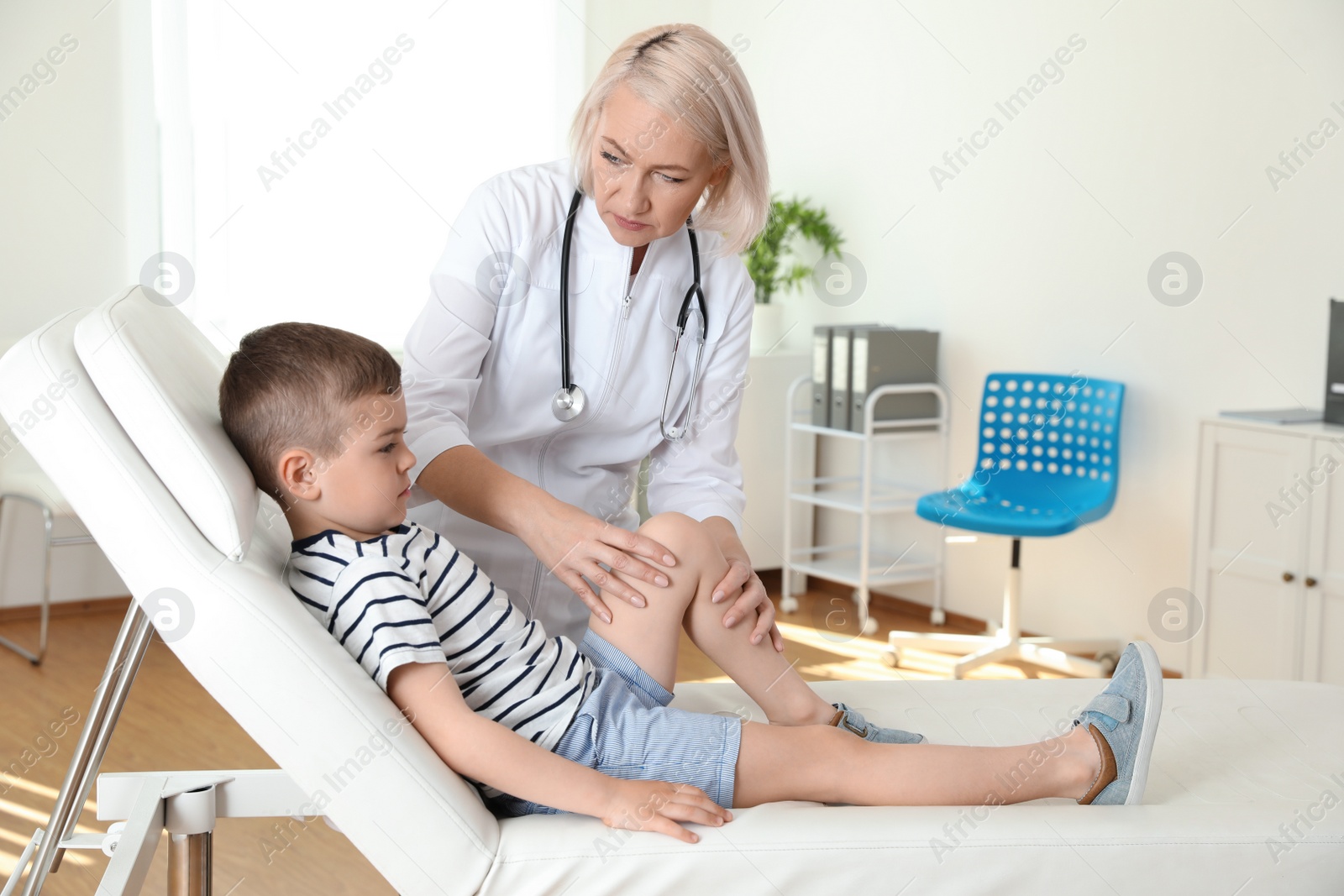 Photo of Doctor examining little patient with knee problem in clinic