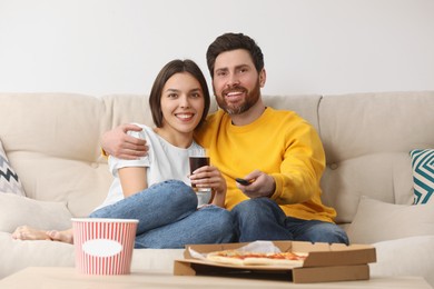 Happy couple watching TV with popcorn and pizza on sofa