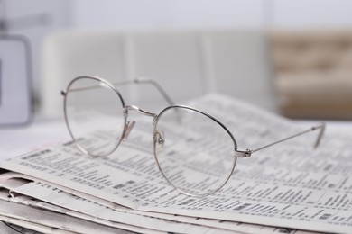 Photo of Glasses on stack of newspapers indoors, closeup