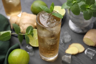 Photo of Glass of tasty ginger ale with ice cubes and ingredients on grey wooden table, closeup