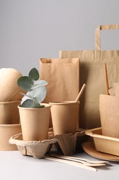 Photo of Eco friendly food packaging. Paper containers, tableware, bag and eucalyptus branch on white table