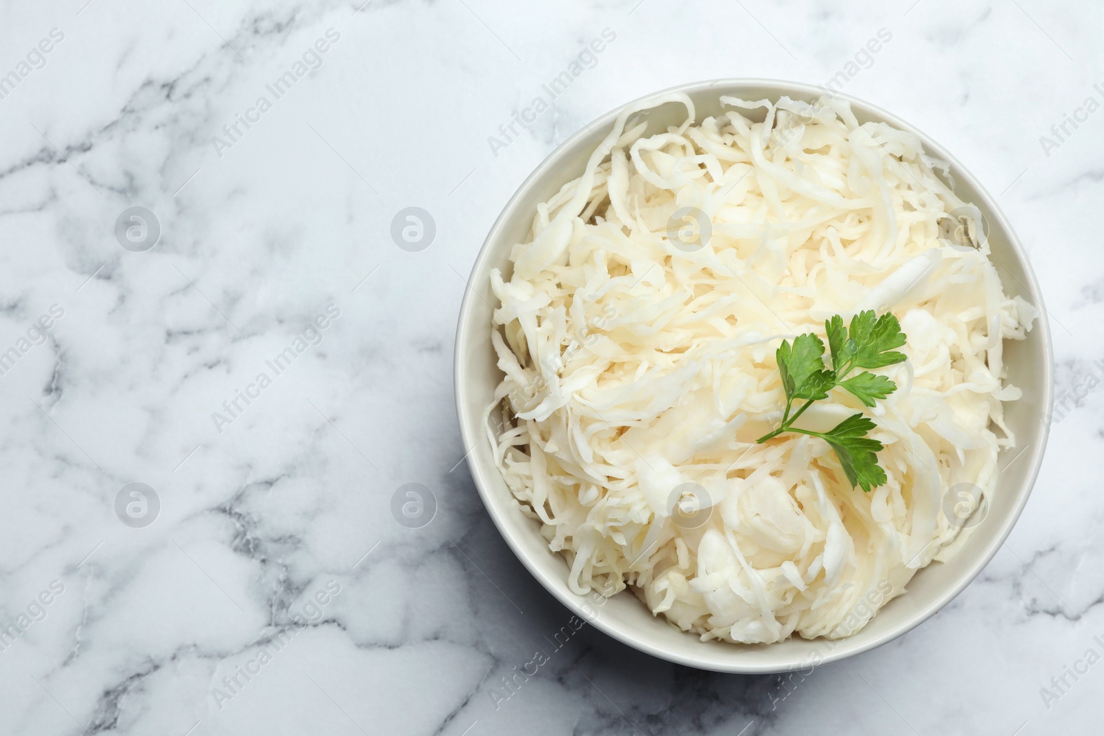 Photo of Tasty fermented cabbage with parsley on white marble table, top view. Space for text