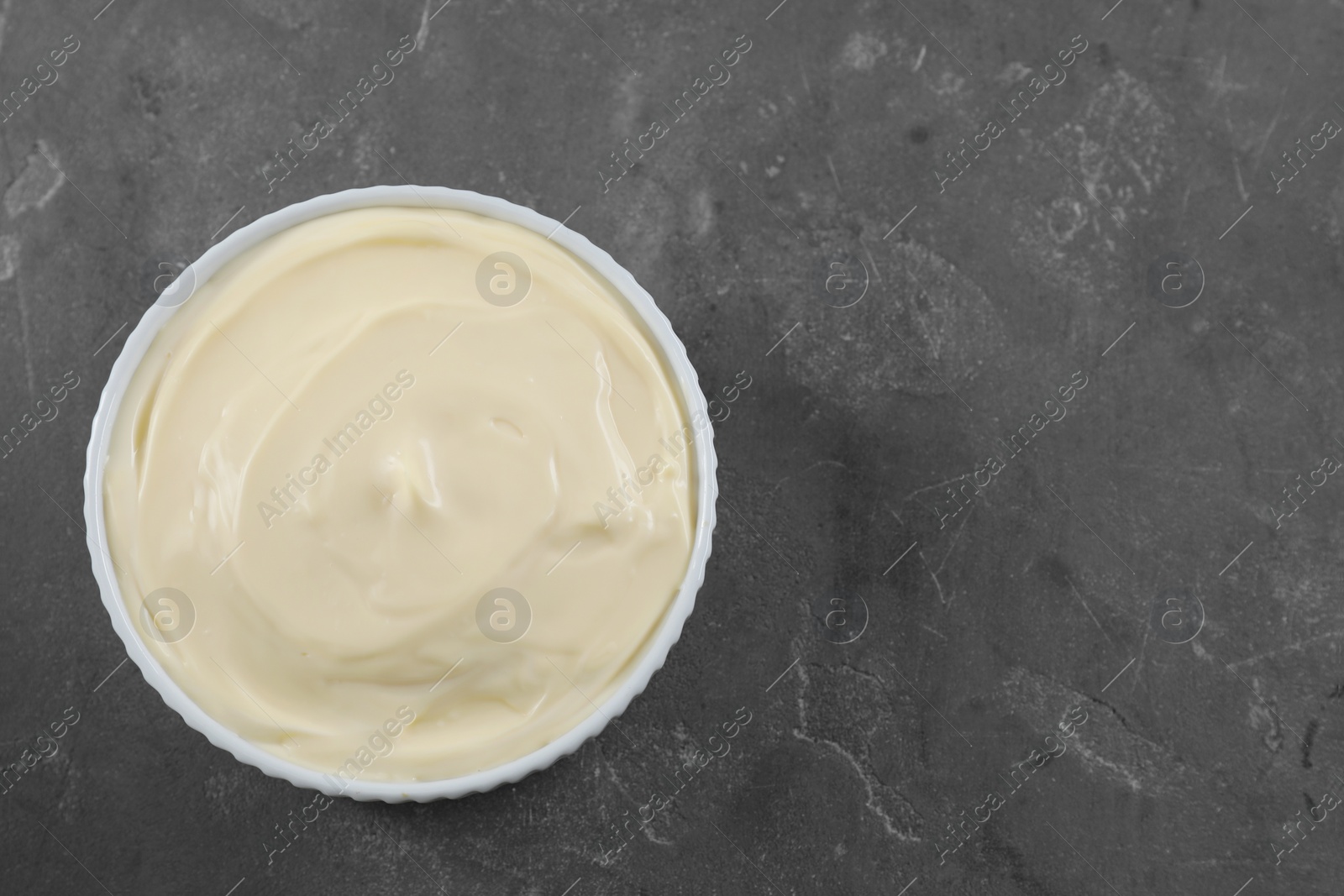 Photo of Fresh mayonnaise sauce in bowl on grey table, top view. Space for text