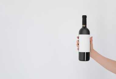 Woman holding bottle of wine on light background