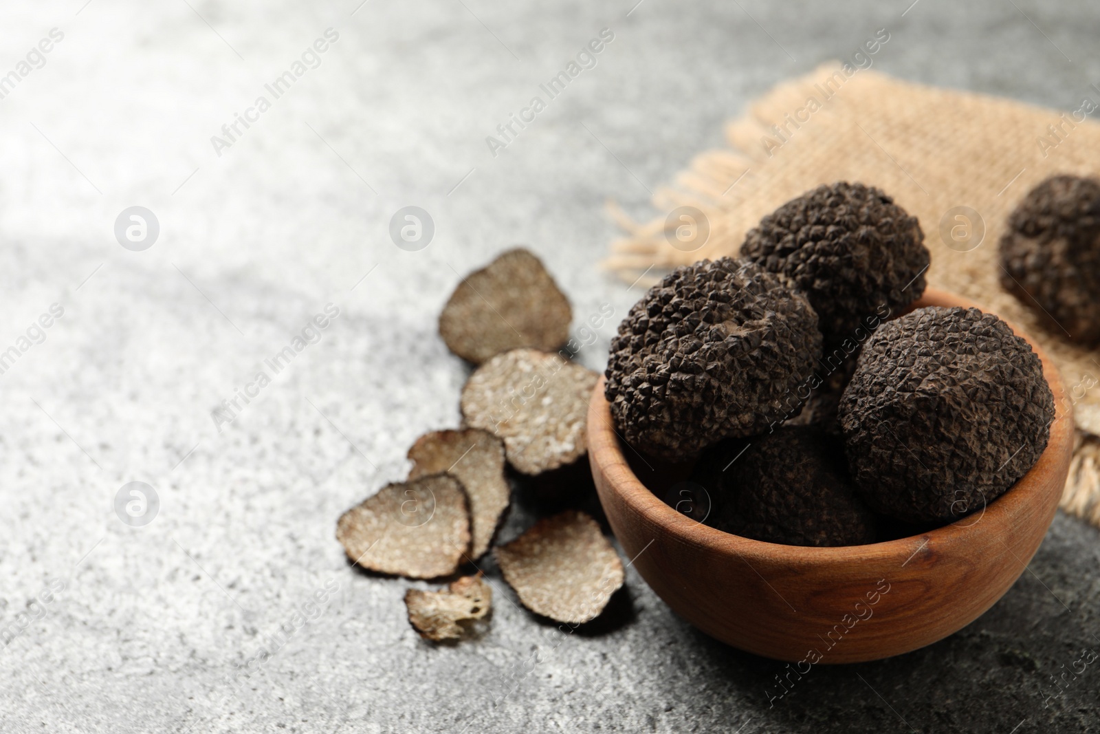 Photo of Black truffles with wooden bowl on grey table. space for text