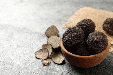 Photo of Black truffles with wooden bowl on grey table. space for text