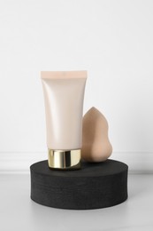 Photo of Tube of skin foundation and sponge near white wall. Makeup product