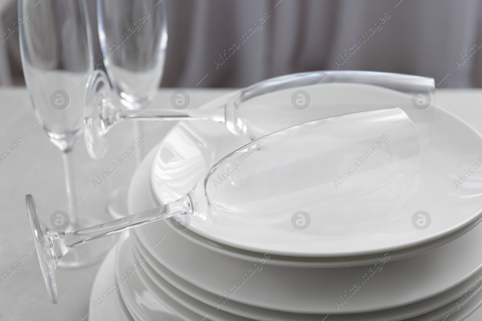 Photo of Stacked plates and glasses on light grey table, closeup