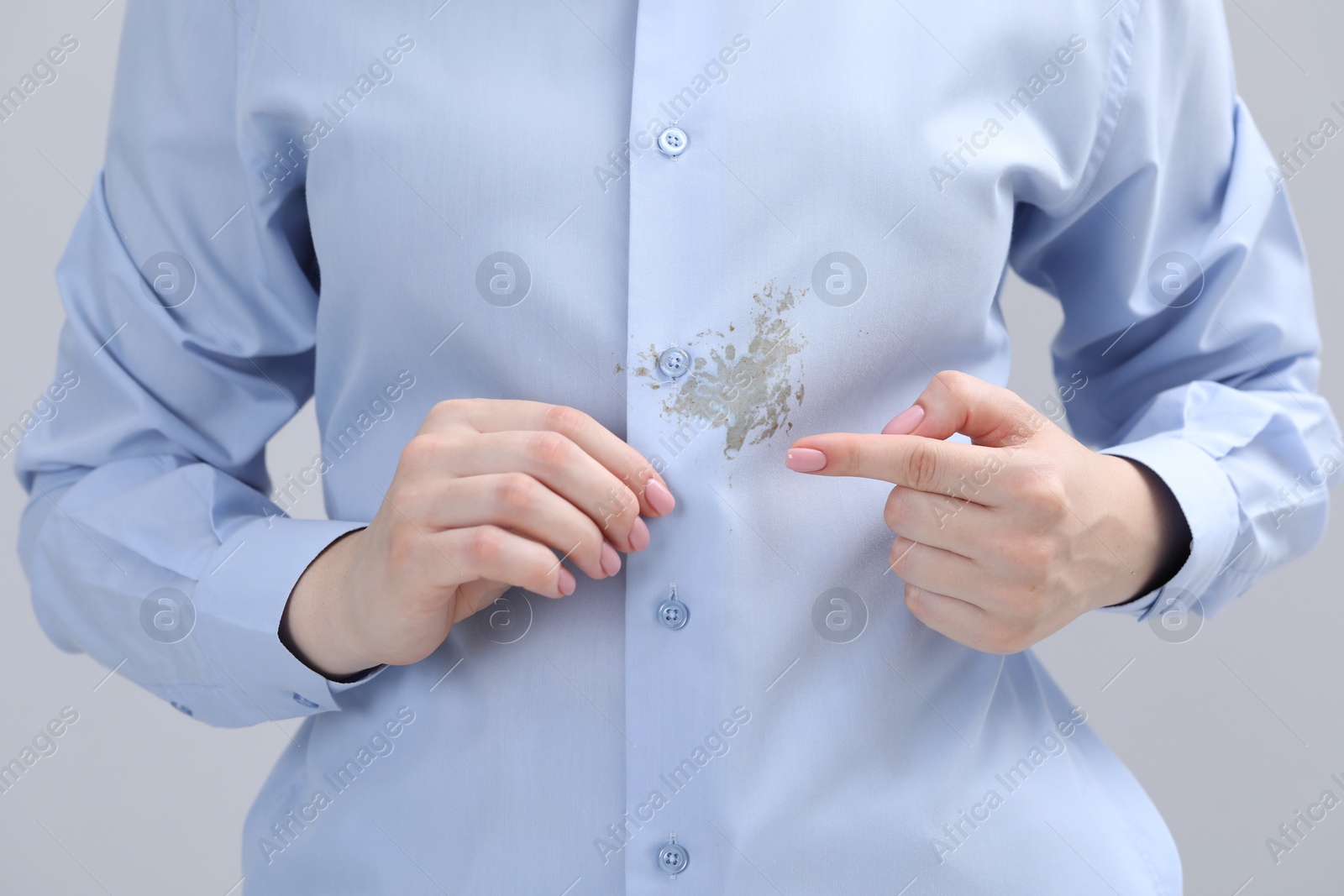 Photo of Woman showing stain on her shirt against light grey background, closeup