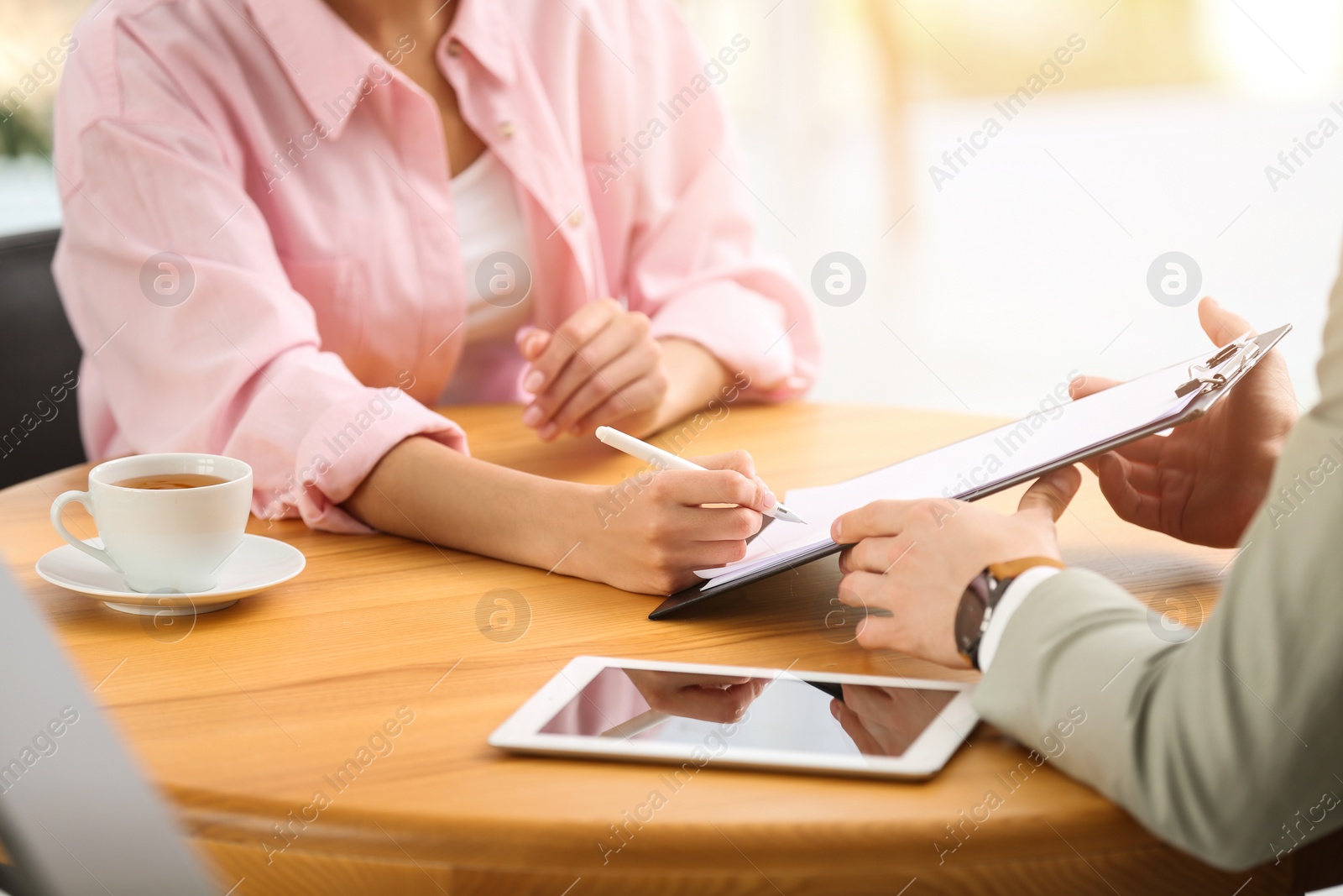 Photo of Woman signing contract with insurance agent in office, closeup