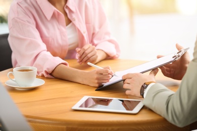 Woman signing contract with insurance agent in office, closeup