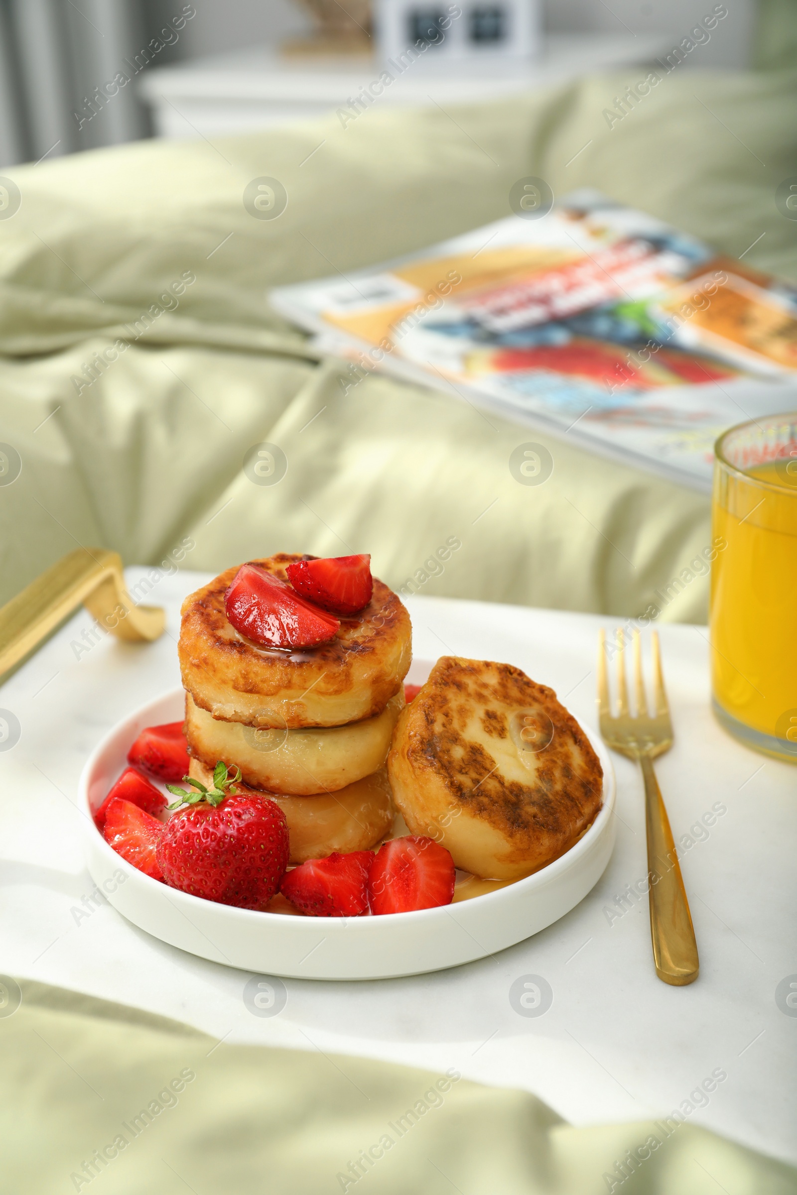 Photo of Tasty breakfast served in bedroom. Cottage cheese pancakes with strawberries and honey on white tray