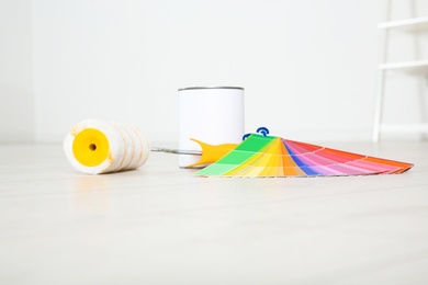 Photo of Can of paint, roller brush and color palette on wooden floor indoors