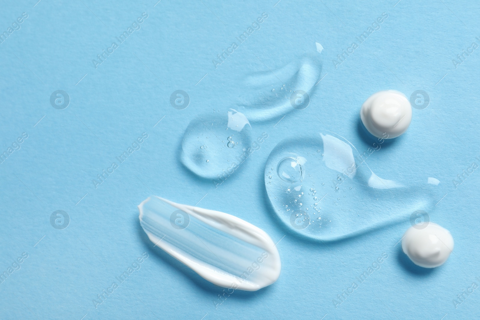 Photo of Samples of transparent gel and white cream on light blue background, flat lay. Space for text