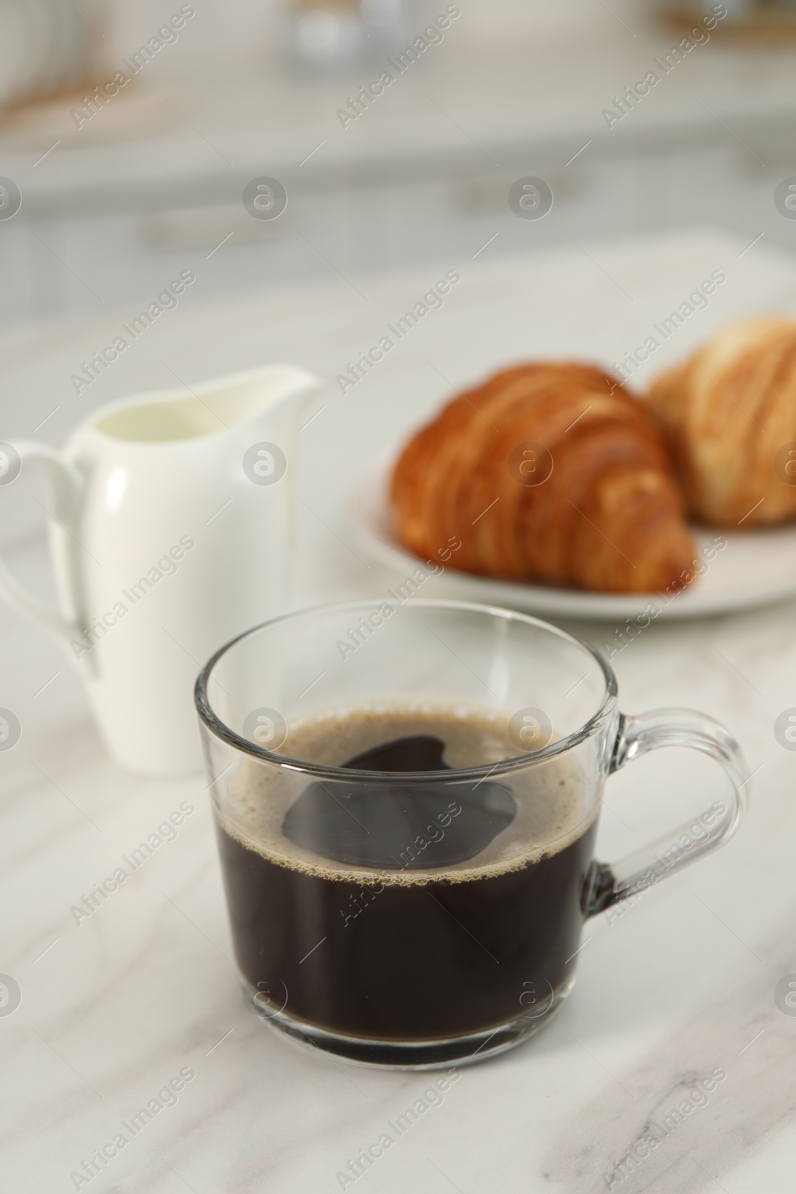 Photo of Aromatic coffee in glass cup, pitcher and fresh croissants on white marble table