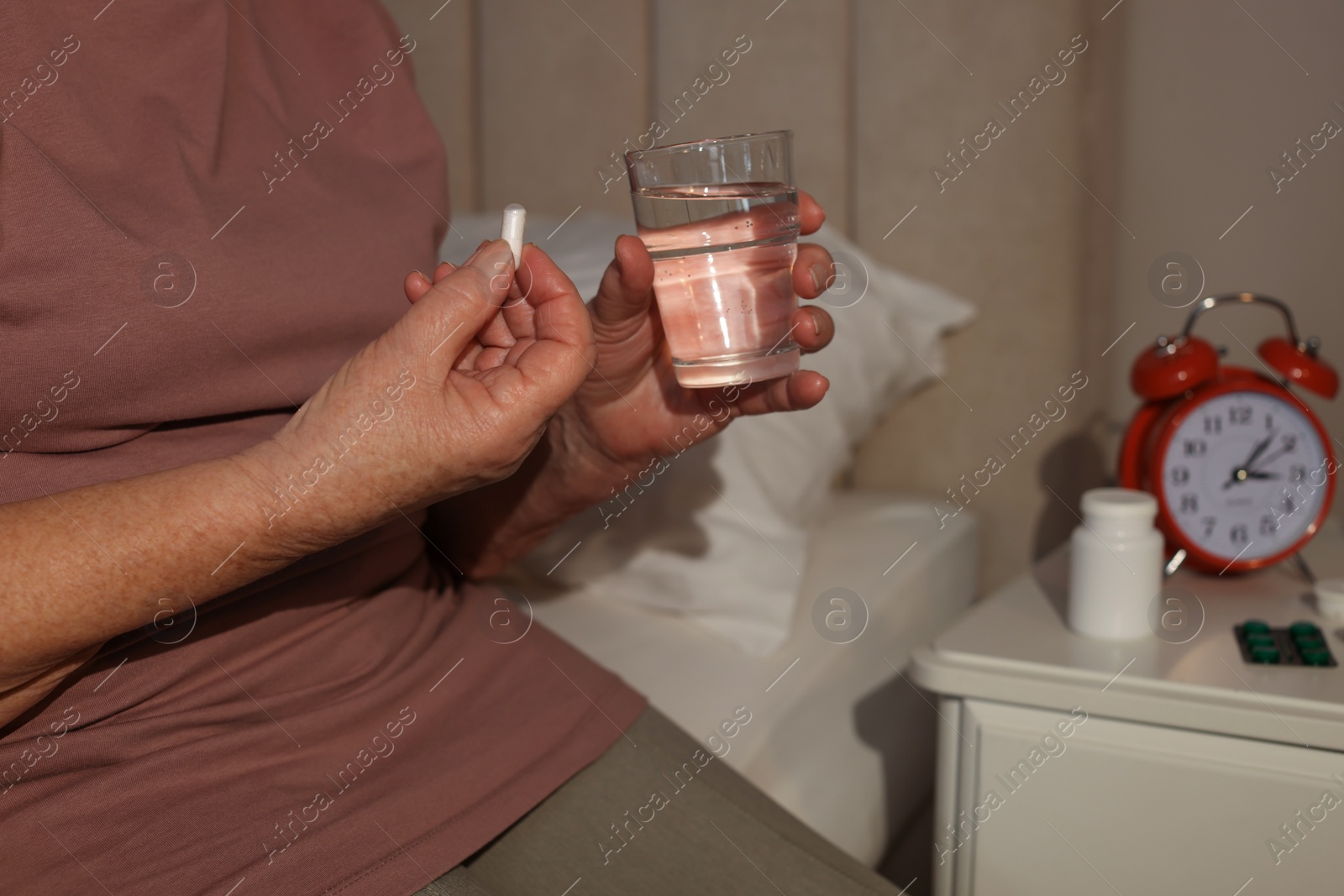 Photo of Elderly woman suffering from insomnia taking pill on bed at night, closeup