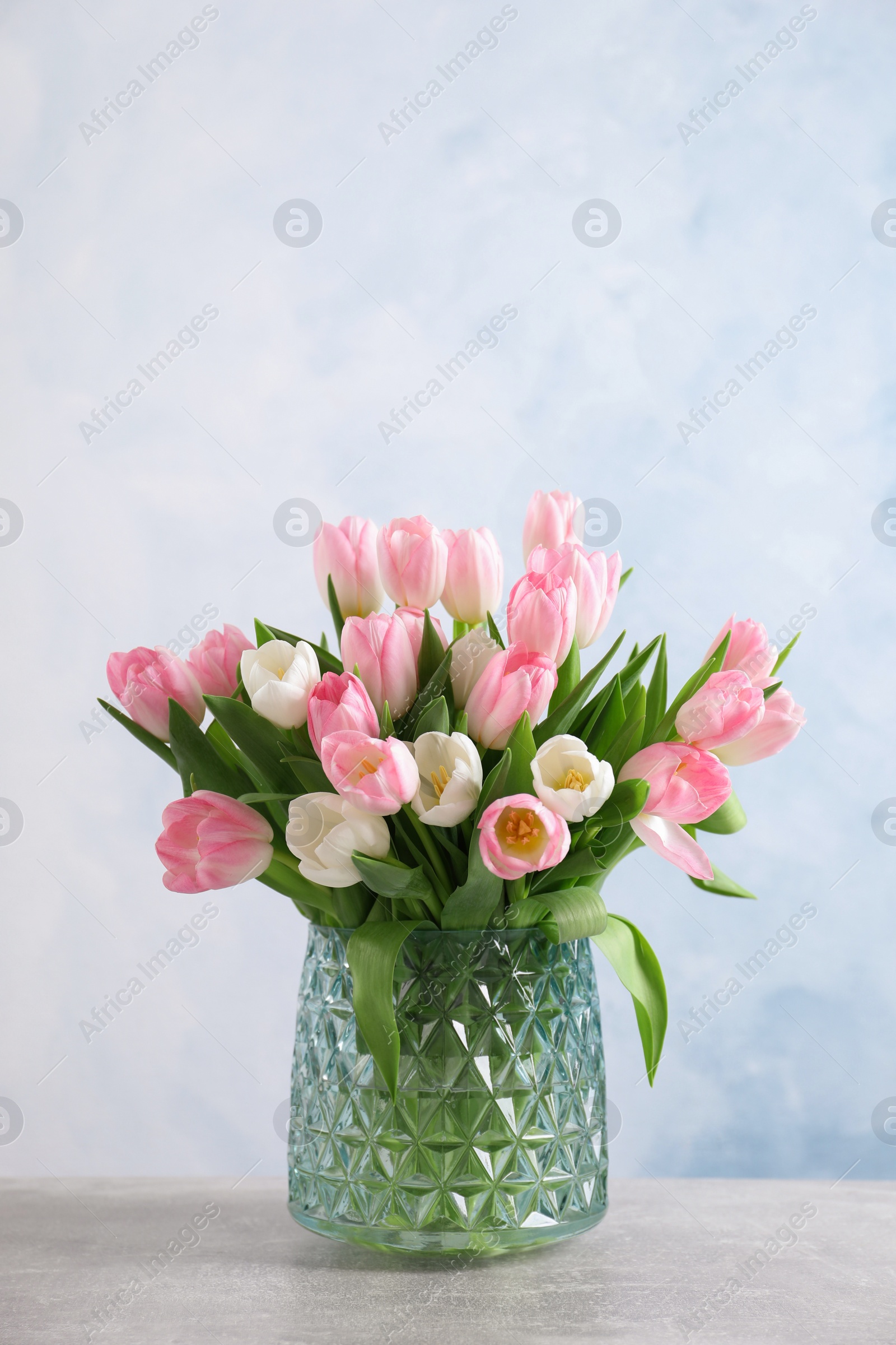 Photo of Beautiful bouquet of tulips in glass vase on light table