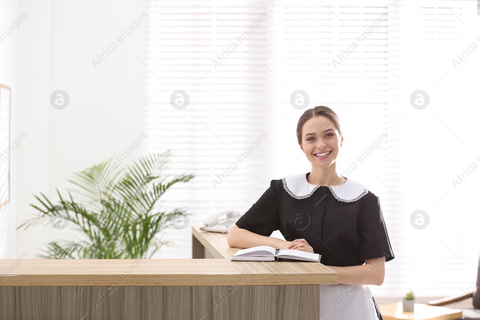 Photo of Young chambermaid near reception in hotel. Space for text