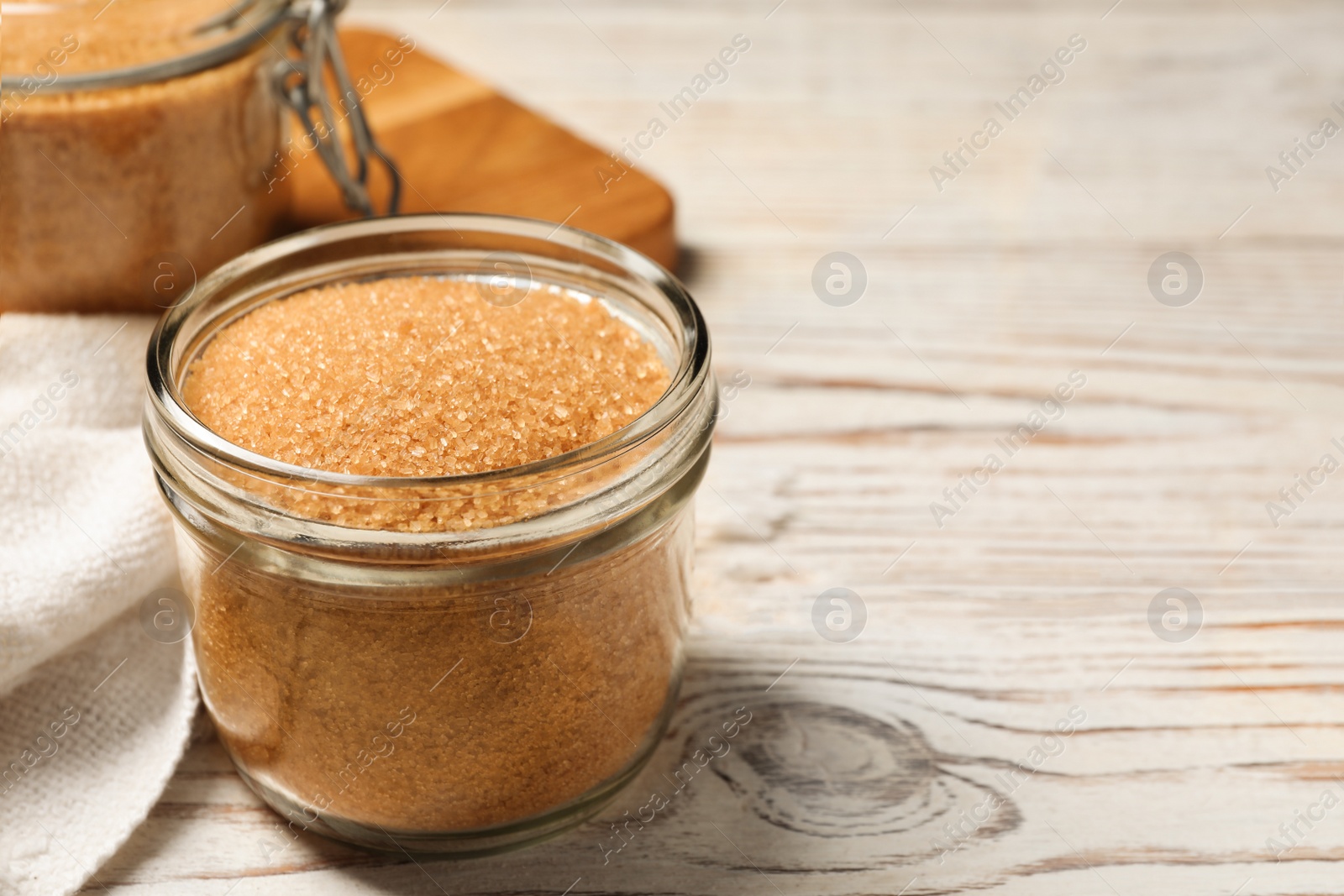 Photo of Glass jar with brown sugar on white wooden table. Space for text