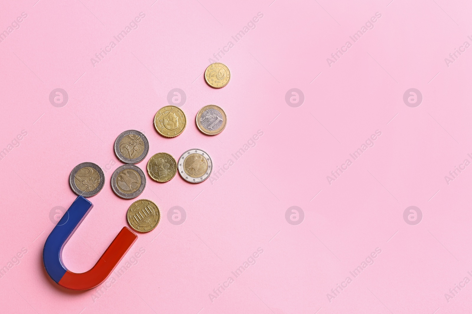 Photo of Red and blue horseshoe magnet attracting coins on pink background, flat lay. Space for text