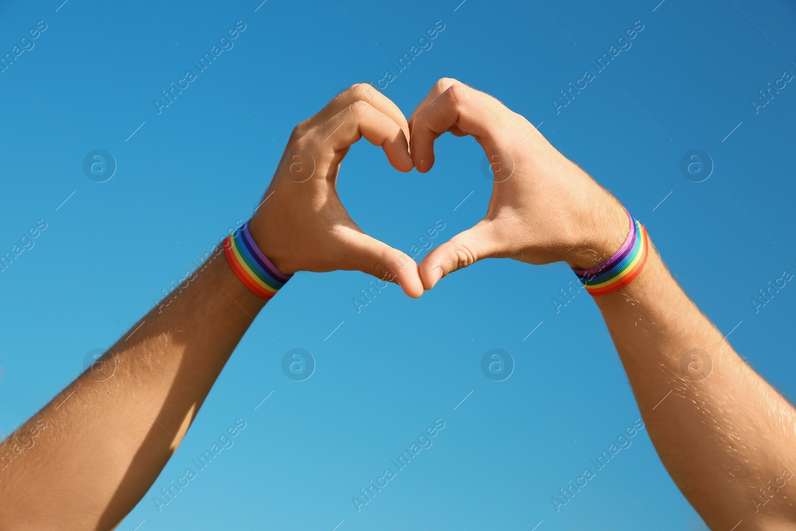 Photo of Gay couple making heart shape with their hands against blue sky, closeup