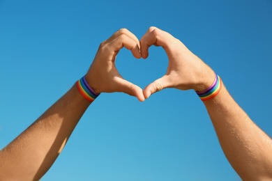 Photo of Gay couple making heart shape with their hands against blue sky, closeup