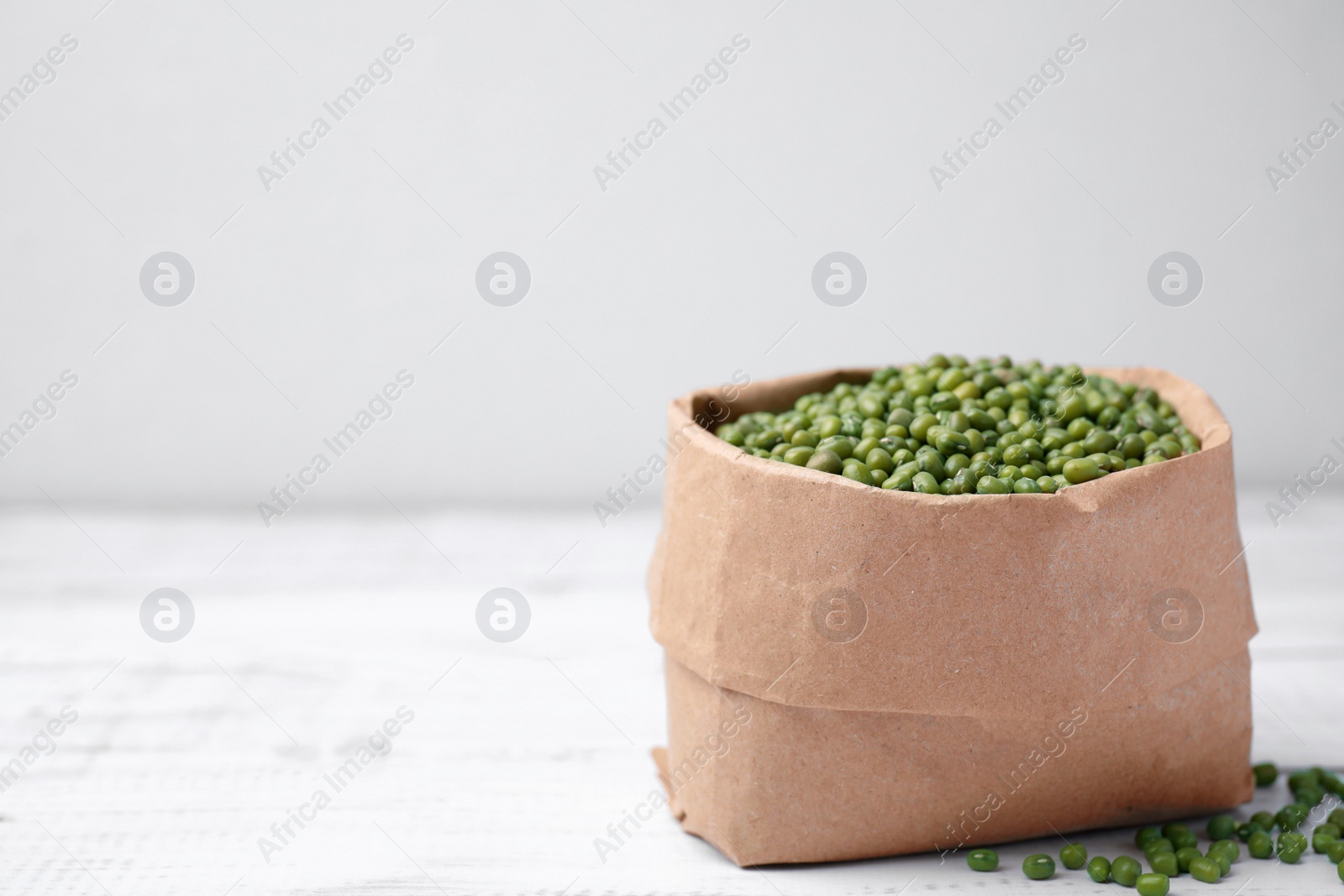 Photo of Paper bag with green mung beans on white wooden table. Space for text