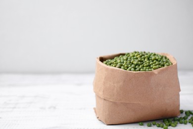 Photo of Paper bag with green mung beans on white wooden table. Space for text