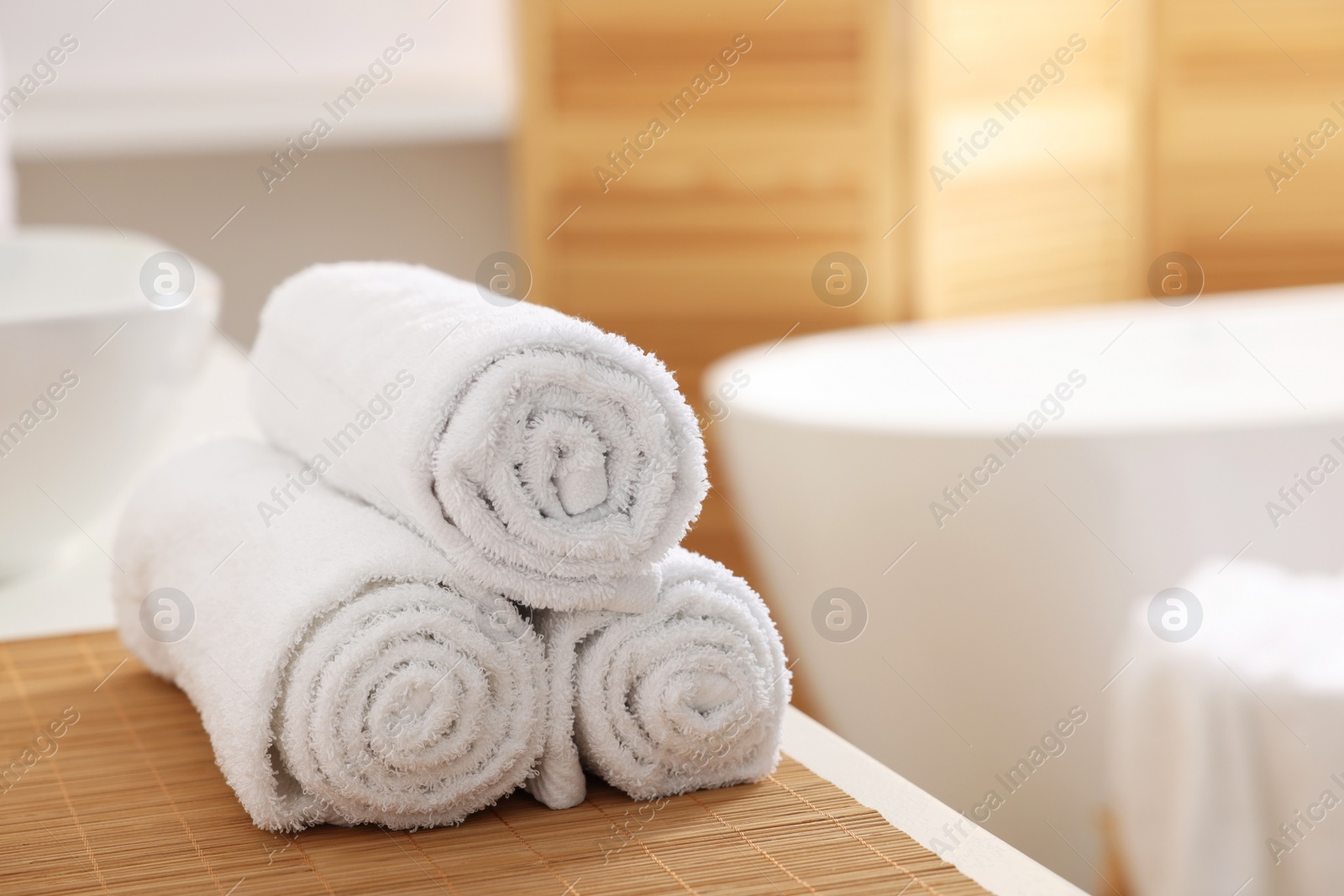 Photo of Rolled soft towels on white table in bathroom. Space for text