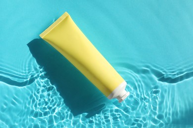 Tube with moisturizing cream in water on light blue background, top view