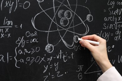 Teacher writing physical formulas with chalk on black chalkboard, closeup