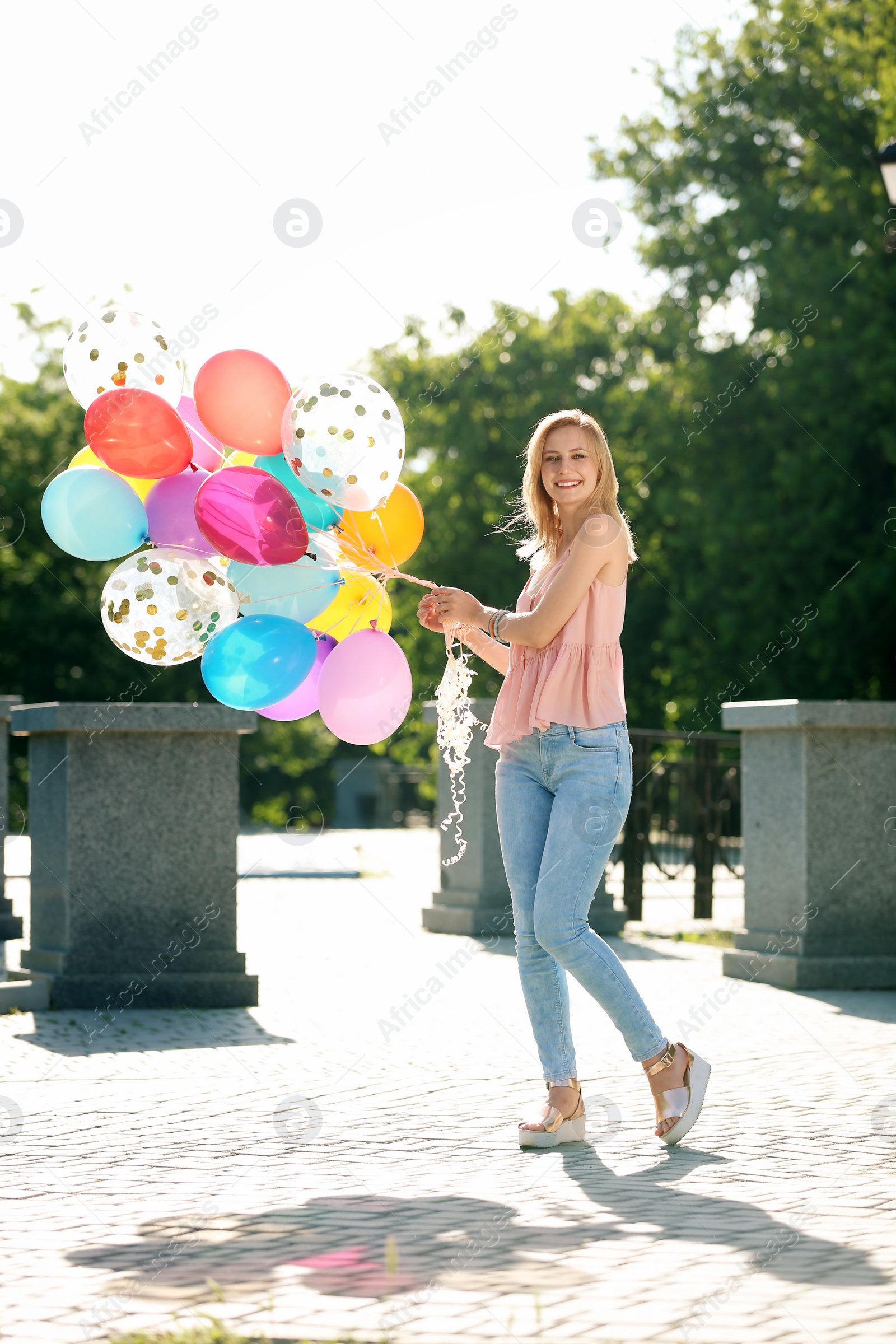 Photo of Young woman with colorful balloons outdoors on sunny day