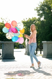 Photo of Young woman with colorful balloons outdoors on sunny day